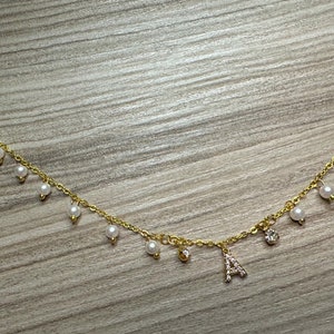 May include: A gold chain necklace with a letter A charm and pearl accents.