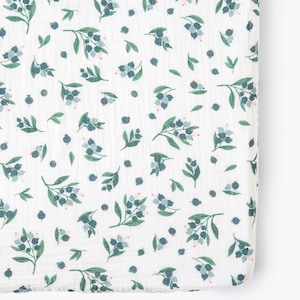 May include: White fitted cot sheet with a repeating pattern of green leaves and blue berries.