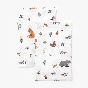 May include: Two white muslin baby burp cloths with a woodland animal print. One cloth features a fox, a bird, and carrots. The other cloth features a squirrel, a badger, and mushrooms.