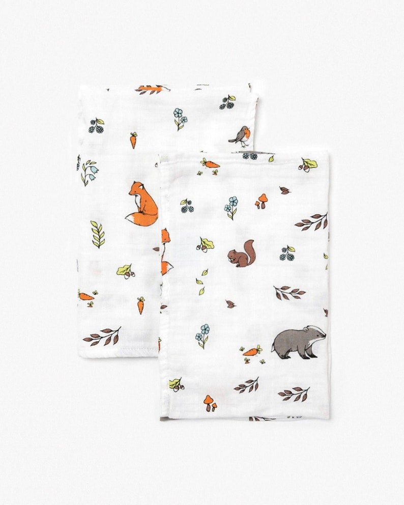 May include: Two white muslin baby burp cloths with a woodland animal print. One cloth features a fox, a bird, and carrots. The other cloth features a squirrel, a badger, and mushrooms.