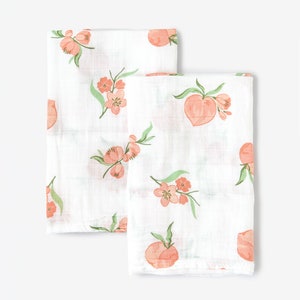 May include: Two white muslin swaddles with a peach and floral print. The swaddles are made of soft, breathable fabric and are perfect for keeping baby warm and cozy.