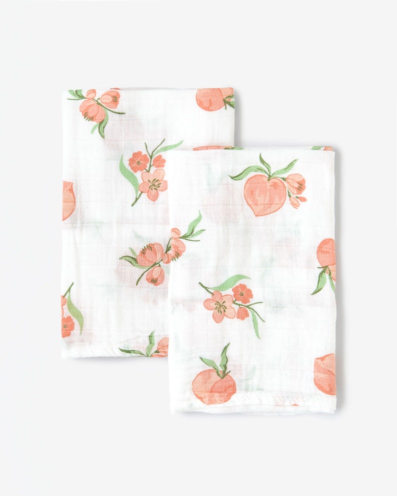 May include: Two white muslin swaddles with a peach and floral print. The swaddles are made of soft, breathable fabric and are perfect for keeping baby warm and cozy.