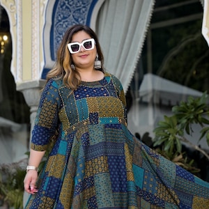 May include: A woman wearing a blue and gold patterned dress with a round neckline and three-quarter sleeves. She is wearing white sunglasses and white shoes.