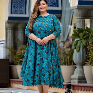 May include: A teal blue dress with a geometric pattern and a round neckline. The dress has 3/4 sleeves and a flared skirt.