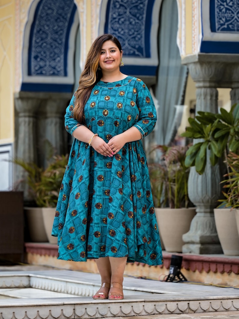 May include: A teal blue dress with a geometric pattern and a round neckline. The dress has 3/4 sleeves and a flared skirt.
