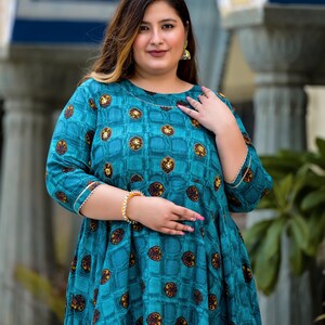 May include: A teal blue dress with a geometric pattern and gold accents. The dress has a round neckline and three-quarter sleeves.
