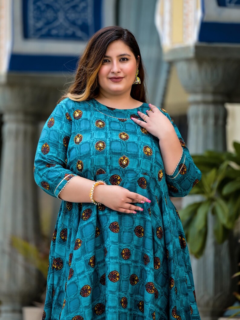 May include: A teal blue dress with a geometric pattern and gold accents. The dress has a round neckline and three-quarter sleeves.