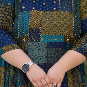 May include: A blue and green patterned dress with gold embroidery and a gold watch on the left wrist.