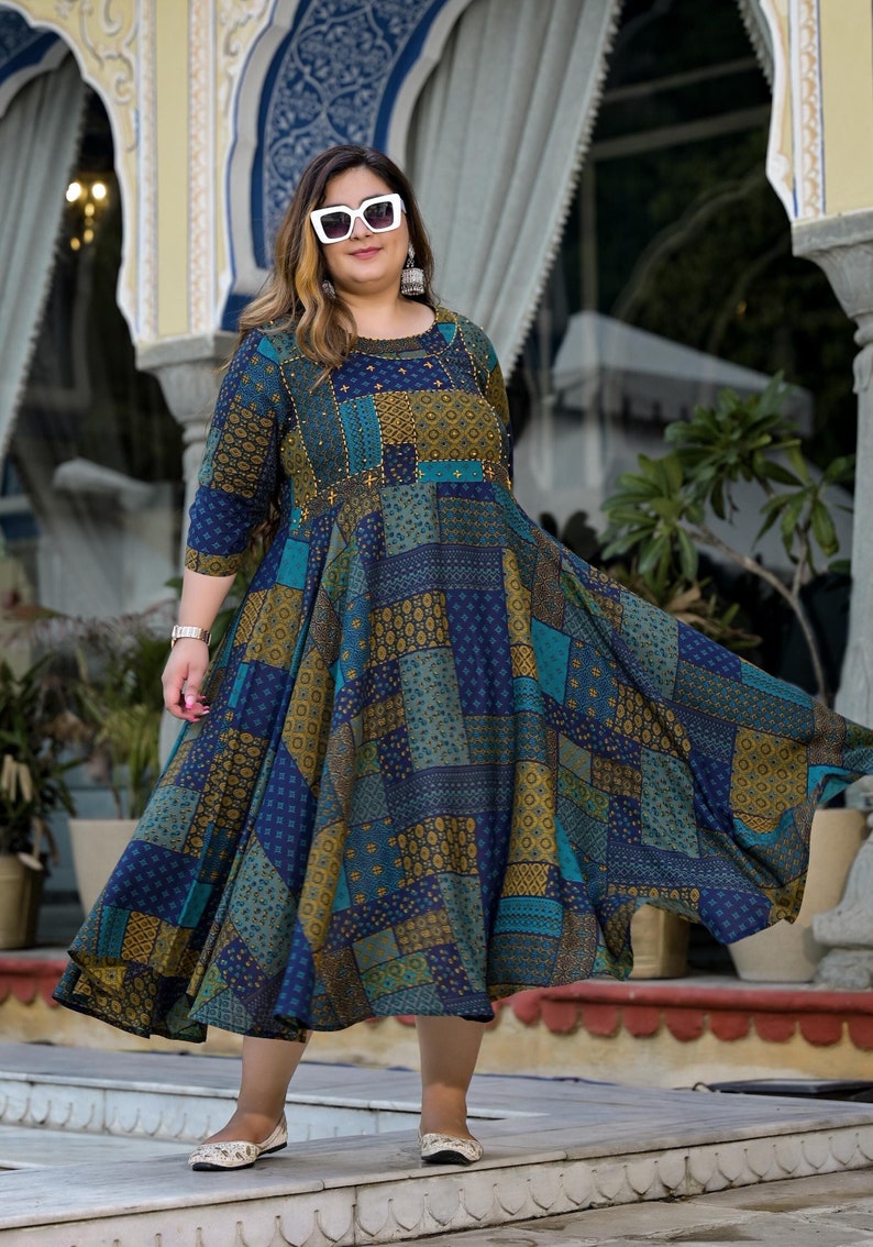 May include: A woman wearing a blue and gold patterned dress with a round neckline and three-quarter sleeves. She is wearing white sunglasses and white shoes.