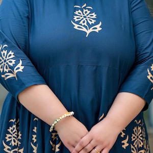 May include: A teal blue maxi dress with gold floral print. The dress has three-quarter sleeves and a round neckline.
