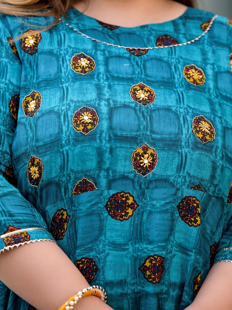 May include: A teal blue dress with a checkered pattern and gold floral embroidery. The dress has a round neckline and three-quarter sleeves.