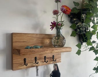 May include: A wooden key holder with four black hooks, a small shelf, and a decorative vase with flowers. Two small green turtle figurines sit on the shelf. Keys hang from the hooks.