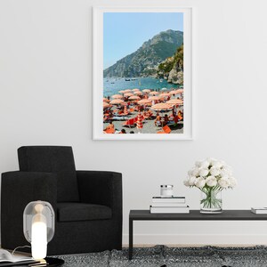 May include: A framed photograph of a beach scene with red and white striped umbrellas and people relaxing on the sand. The beach is located on a coastline with a mountain in the background.