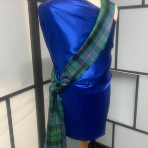 May include: A blue satin fabric with a green, red, and blue plaid sash tied around it. The sash is tied in a knot at the waist and the ends are hanging down.