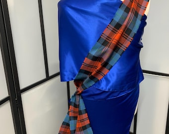 May include: A blue satin dress with a plaid sash tied around the waist. The sash is red, black, and blue.