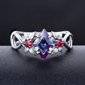 May include: A silver ring featuring a square-shaped purple and blue gemstone, flanked by two red pear-shaped gemstones and silver leaf designs.