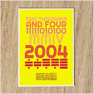 May include: A yellow poster with the year 2004 written in different ways, including the words "Two Thousand and Four", the binary code "11111010100", the Roman numeral "MMIV", and the number "2004" in large red font. The text "However you write it this year was special Sandra Newcastle 19th September" is at the bottom of the poster.