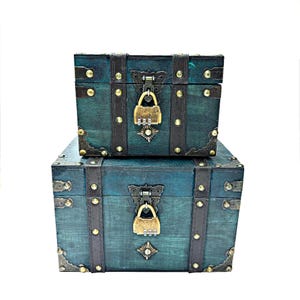 May include: Two teal blue wooden treasure chests with ornate brass hardware and locks. The chests are stacked on top of each other.