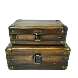 May include: Two wooden boxes with brass accents and latches. The boxes are stacked on top of each other. The top box is slightly larger than the bottom box.