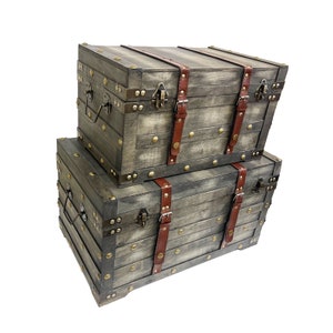 May include: Two stacked wooden storage chests with distressed gray paint, brown leather straps, and brass accents.
