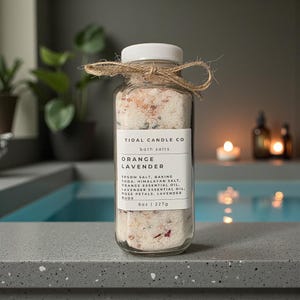 May include: A clear glass jar of Tidal Candle Co. Orange Lavender bath salts, tied with twine. The label lists ingredients like Epsom salt and orange essential oil. The jar contains 8 oz (227g) of bath salts, with visible pink rose petals.