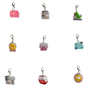 Puede incluir: Una colección de nueve colgantes coloridos con cierres plateados. Los colgantes presentan varios diseños, incluyendo un cuadrado rosa con el texto "I'M FINE IT'S JUST MY FACE", un dinosaurio verde y un cartón de leche rojo y blanco.