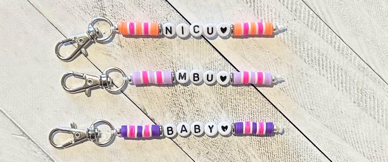 Puede incluir: Tres llaveros de cuentas con cierres plateados. Cada llavero tiene una palabra diferente escrita con cuentas de letras blancas: NICU, MBU y BABY. Los llaveros presentan cuentas a rayas de colores en tonos de rosa, morado y naranja, con cuentas en forma de coraz&oacute;n.