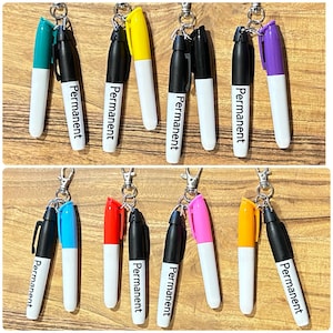 May include: A collection of colorful permanent marker keychains. Each keychain features a black marker paired with a marker in a different color, including teal, yellow, purple, blue, red, pink, and orange. The word "Permanent" is printed on each marker.