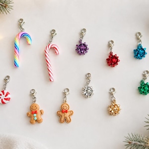 May include: A collection of eleven holiday-themed charms featuring two candy canes, two gingerbread figures, a red and white peppermint candy, and six metallic gift bows in purple, red, blue, silver, gold, and green, each with a silver lobster clasp.