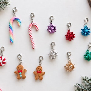 May include: A collection of ten Christmas-themed charms with silver lobster clasps. The set includes two candy canes, two gingerbread people, a peppermint disc, and five star-shaped gift bows in purple, red, blue, silver, gold, and green.