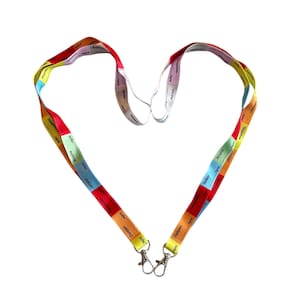 May include: Two colourful lanyards with metal clasps, arranged in a heart shape against a white background. The lanyards are segmented with various colours and text. The text is in a small font and is difficult to read.