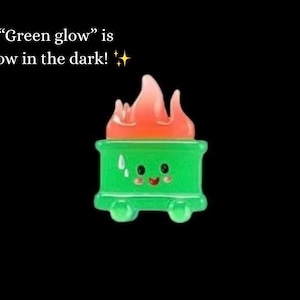 Może przedstawiać: Zielony, kresk&oacute;wkowy pojemnik na śmieci z uśmiechniętą twarzą i pomarańczowymi płomieniami na g&oacute;rze. Tekst "Green glow" is glow in the dark!" jest wyświetlany nad pojemnikiem na czarnym tle.