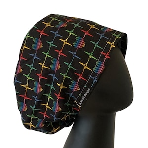 May include: Black scrub hat with a rainbow heart beat pattern. The hat has the text "Little Designs" on the side.