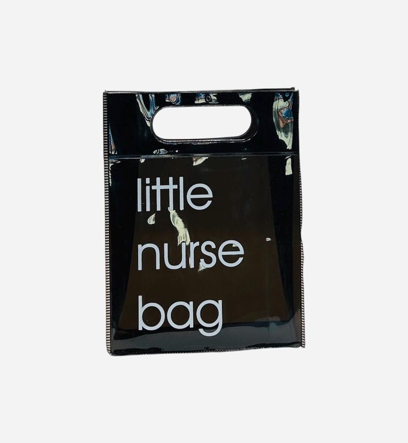 May include: A black, glossy tote bag with a rectangular handle opening at the top. The words "little nurse bag" are printed in white, centered on the front of the bag. The bag has a shiny, reflective surface.