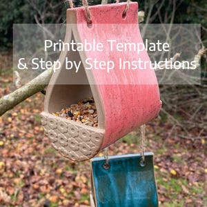 May include: Two handmade ceramic bird feeders hanging from twine. The top feeder is red with a floral pattern on the base and filled with birdseed. The bottom feeder is teal. Text on the image reads "Printable Template & Step by Step Instructions."