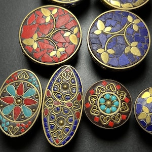 May include: Close-up of several decorative cabinet knobs with mosaic designs. The knobs feature red, blue, and turquoise mosaic tiles set in brass-colored metal. Some have floral patterns, while others have geometric shapes. The knobs are round and oval.