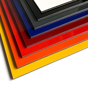 May include: A stack of colorful, glossy aluminum composite panels. The panels are arranged in a diagonal pattern, showcasing a range of vibrant colors including yellow, orange, red, blue, and black. The edges reveal a black core.