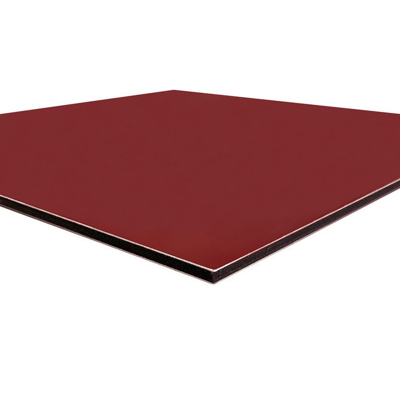 May include: A burgundy-colored square panel with a glossy finish. The panel has a black edge and a white core, creating a layered effect. The surface is smooth and reflects light, suggesting a modern design.