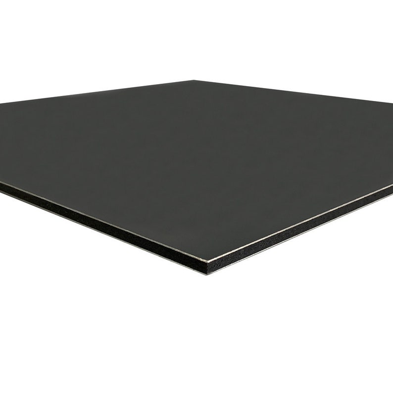 May include: A square, dark gray panel with a smooth, matte finish. The edges are framed with a thin silver border and a black core. The panel appears to be made of a composite material.