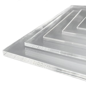 Peut inclure: Quatre plateaux carrés en acrylique transparent empilés les uns sur les autres. Les plateaux sont de tailles différentes, le plus grand plateau étant en bas et le plus petit en haut.