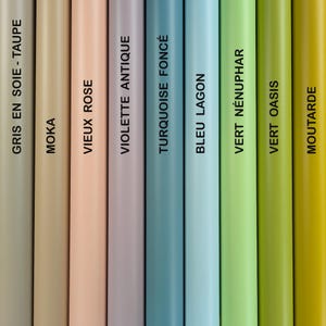 K&ouml;nnte beinhalten: Nahaufnahme von neun zylindrischen Objekten in einer Reihe, jede in einer anderen Farbe. Die Farben umfassen Taupe, Beige, Hellrosa, Lavendel, T&uuml;rkis, Hellblau, Hellgr&uuml;n, Limettengr&uuml;n und Gelb. Jedes Objekt hat eine Farbbezeichnung.