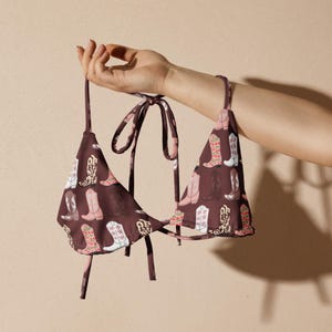 May include: A brown bikini top with a repeating pattern of colorful cowboy boots. The bikini top has tie straps and a triangle shape. The boots are in shades of pink, white, and green.