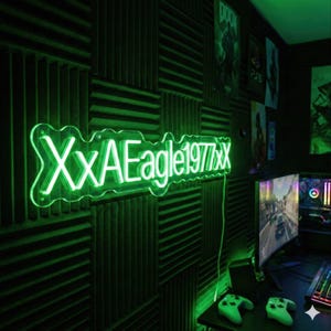 May include: A neon green sign with the text "XxAEagle1977xx" is mounted on a wall covered in dark green acoustic foam panels. The room is lit with green light, and a computer setup with controllers is visible.