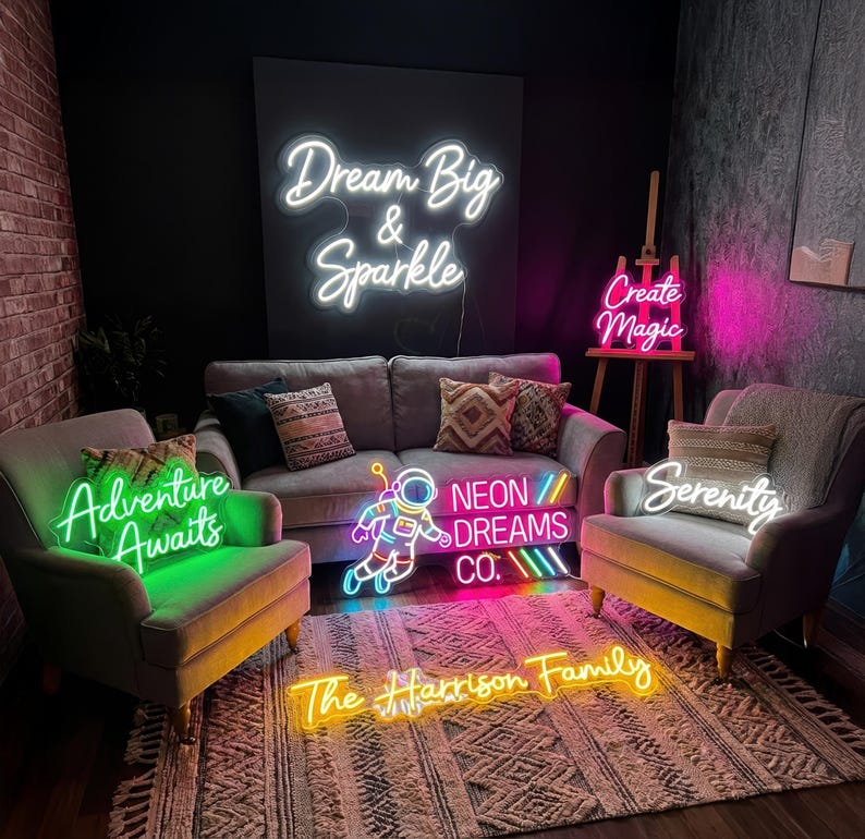 May include: A room with several neon signs. The signs include the phrases "Dream Big & Sparkle", "Create Magic", "Adventure Awaits", "Serenity", "Neon Dreams Co.", and "The Harrison Family". The signs are in various colors, including white, pink, green, and yellow.