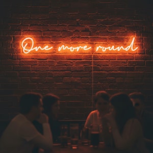 May include: Neon sign with the words "One more round" in a cursive font, mounted on a brick wall. The sign glows orange. People are seated at a table in the foreground.