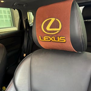 May include: Brown car seat headrest with a brown and yellow embroidered Lexus logo.