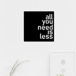 Könnte beinhalten: Ein schwarzes quadratisches Schild mit weißem Text, auf dem "all you need is less" steht, hängt an einer weißen Wand über einem weißen Schreibtisch mit einem weißen Stuhl und einer Topfpflanze.