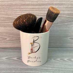 May include: White ceramic makeup brush holder with a black and white design of a stylised letter B with makeup brushes and lipstick. The holder has the text "Becky's Brushes" printed on the front.