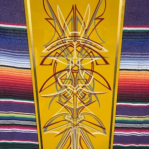 May include: A yellow rectangular artwork with a gold border features a symmetrical design of white, gray, and maroon lines. The artwork is displayed on a black easel against a colorful striped background. The bottom right corner has the text "Togel Bill".