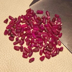 Peut inclure: Une collection de pierres précieuses rubis brutes et non taillées. Les rubis sont d'une couleur rouge profond et vibrante, avec un aspect légèrement translucide. Ils sont de forme irrégulière, avec une texture rugueuse et naturelle. Un outil en métal est en arrière-plan.